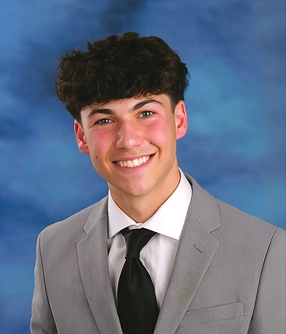 Brandon Zeller in a grey suit against a blue studio backdrop
